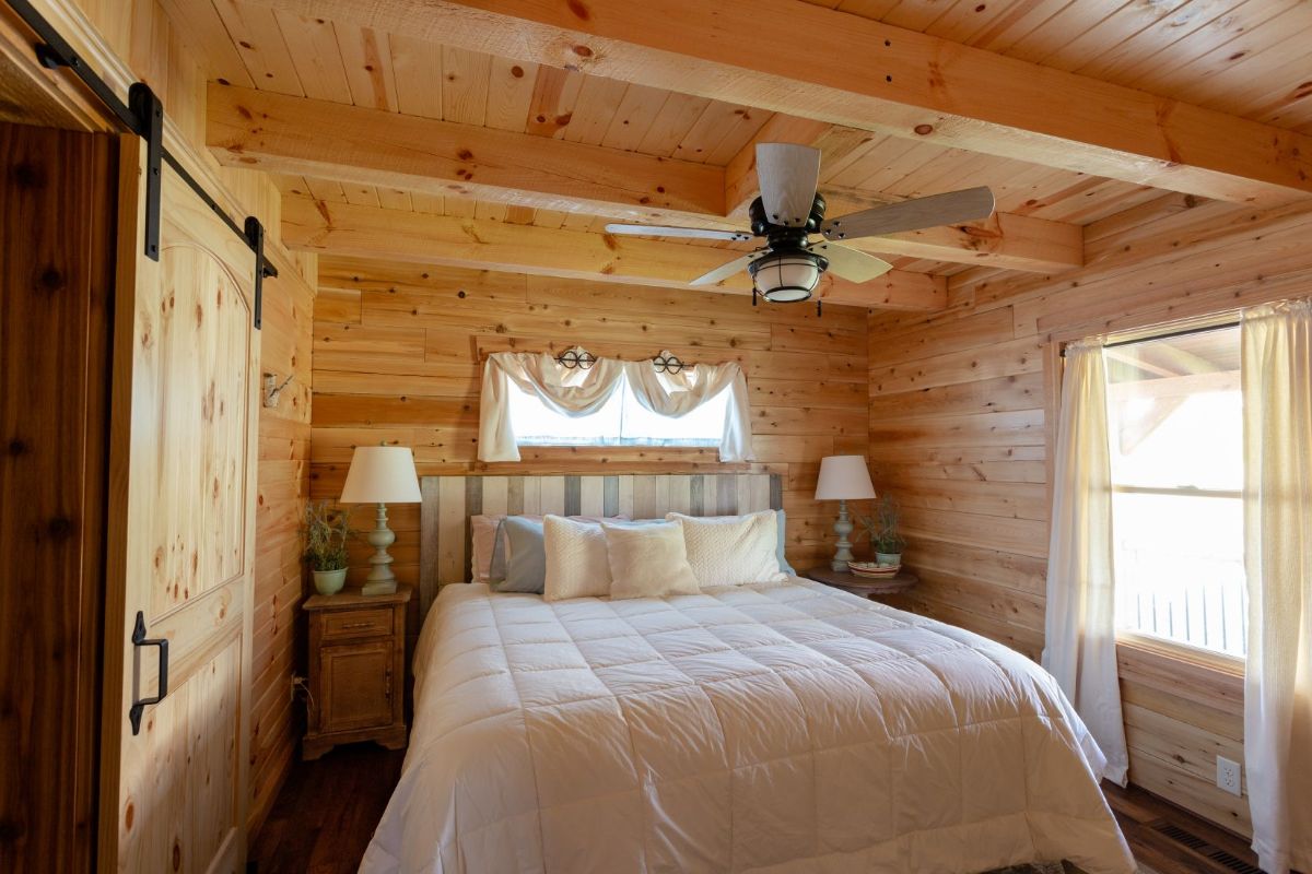 white linens on bed in log cabin room with ceiling fan above bed