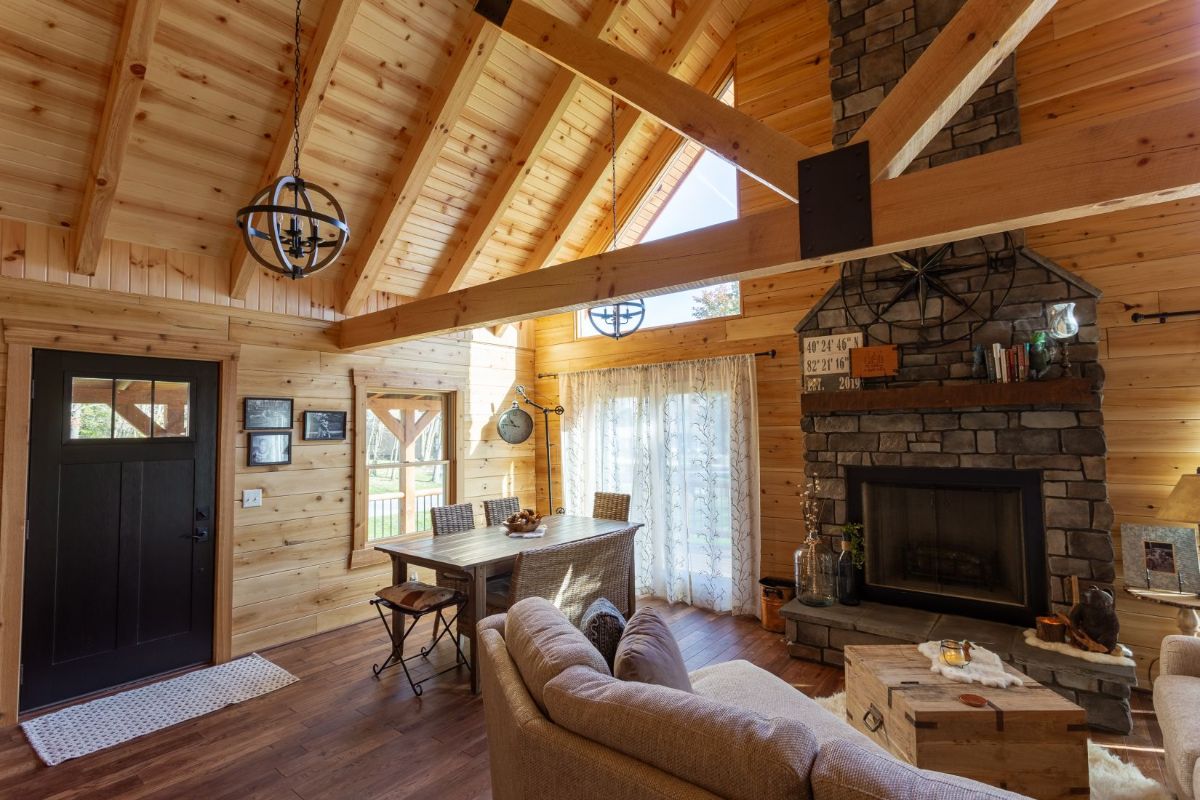 beige sofa in front of log cabin with table and hairs in left background