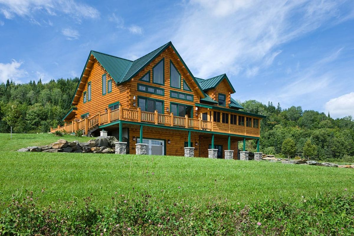 light wood log cabin with green trim and roof and stone columns on back of home