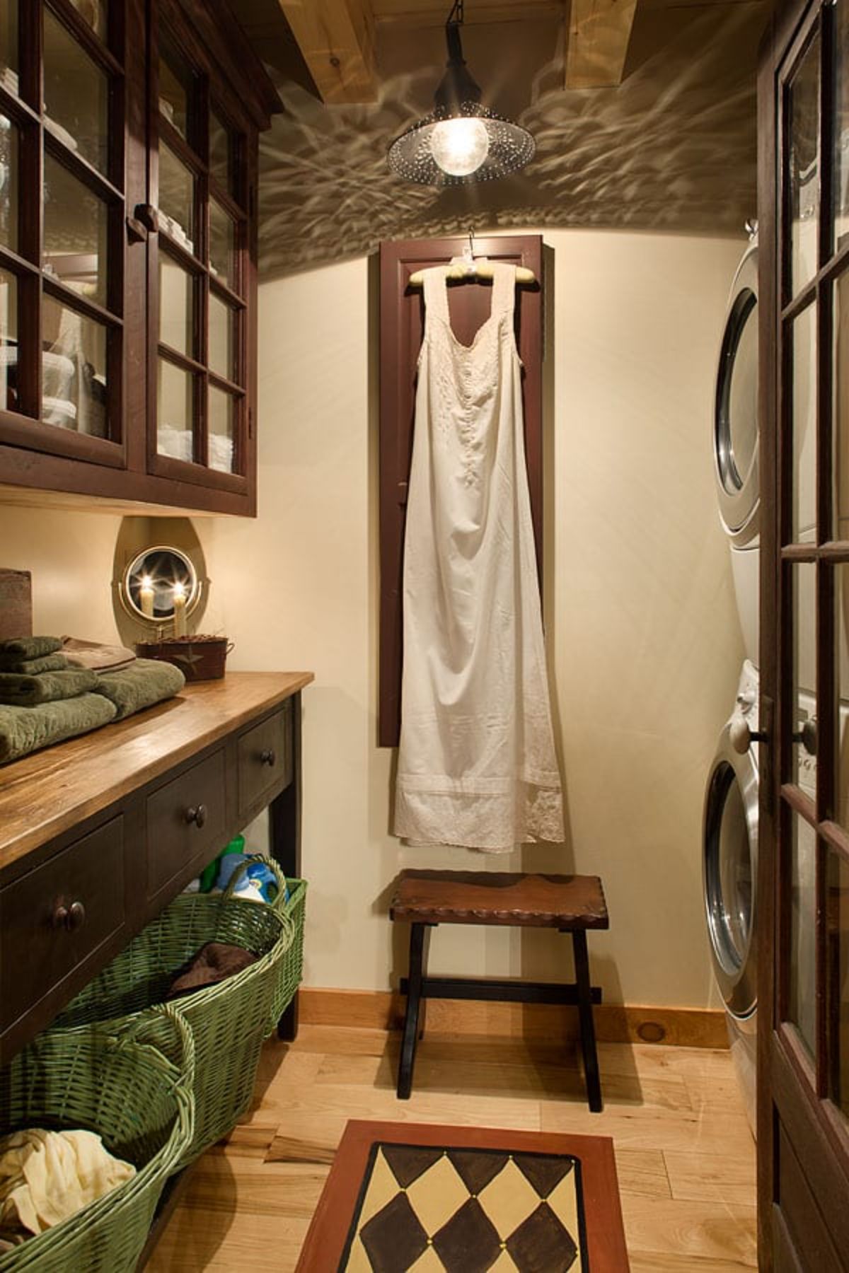 white gown hanging on wall behind stool in room with stacking laundry setup on right and sink on left