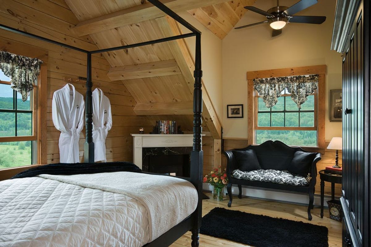 blck metal four poster bed with white bedding in front of small fireplace in bedroom with black sofa under window