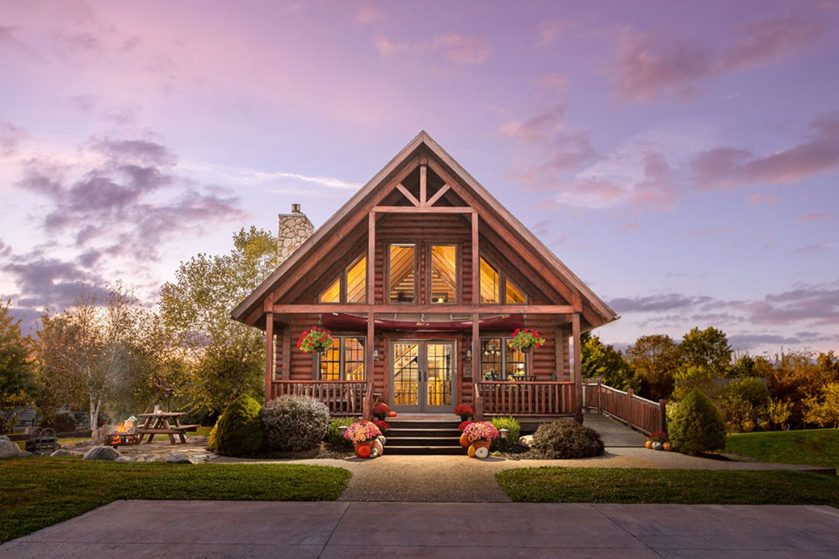 front of log cabin with wall of windows and purple sky background