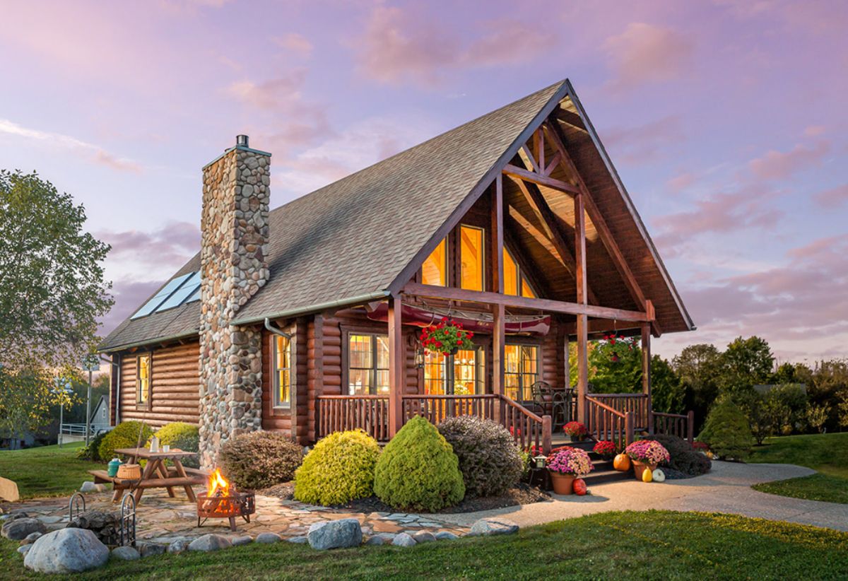 stone chimney on front side of log cabin with green shrubs out front