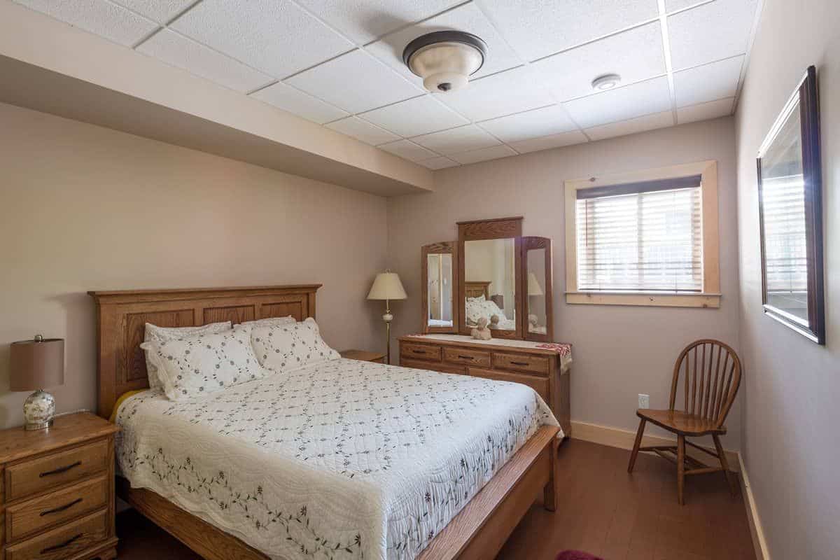 white bedding on wood bed frame in bedroom with dresser against wall and light cream walls