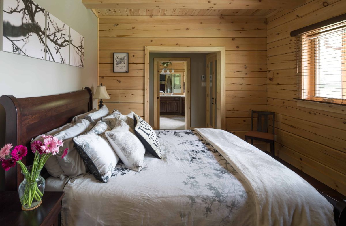 light wood bedding on bed in log cabin bedroom with light wood walls on back wall