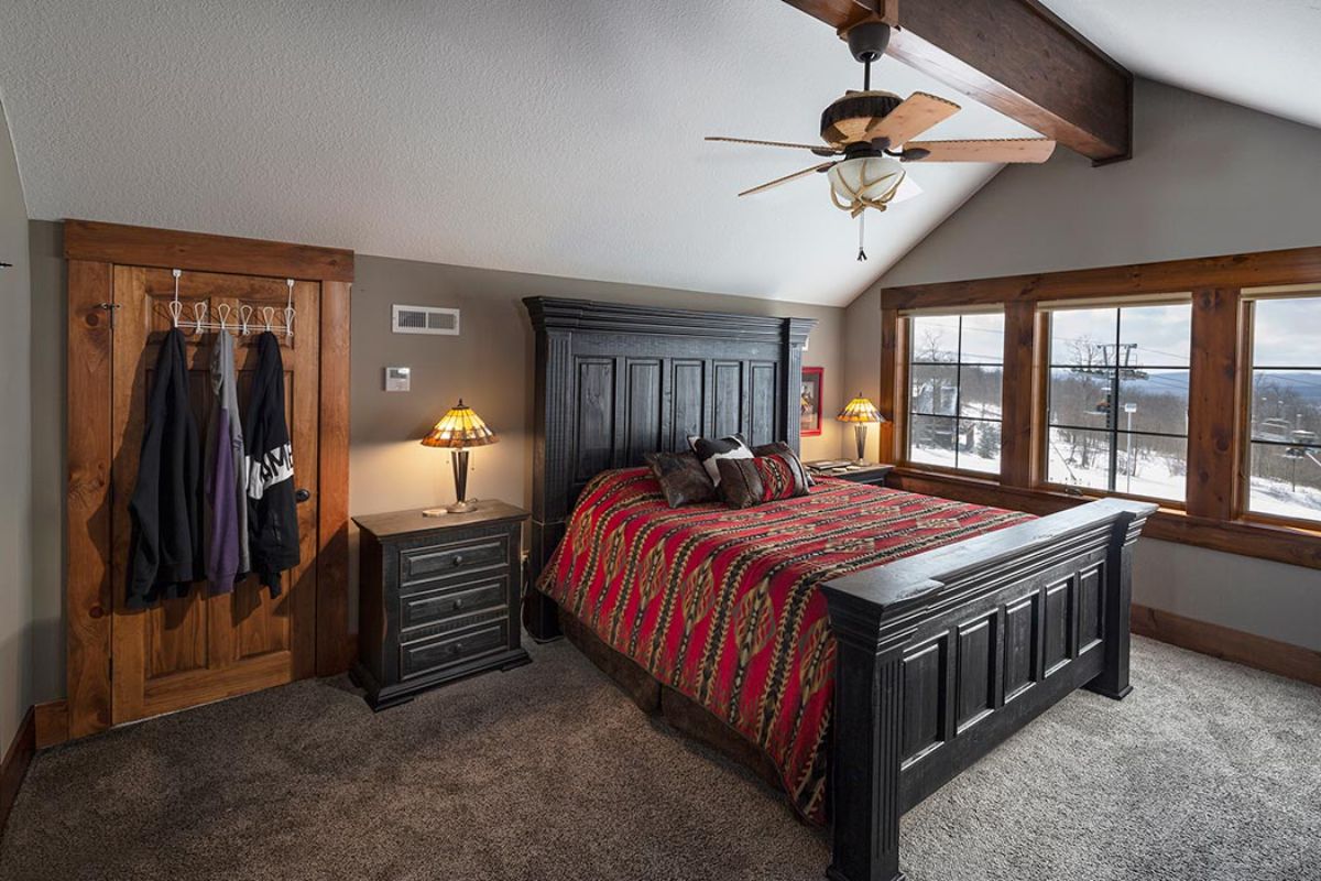 black bedframe with red comforter on bed with wall of windows on far right side