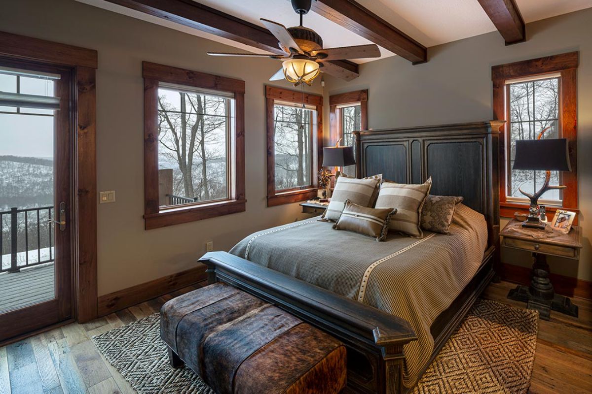 gray bedding on black bedframe with trunk at end of bed in log cabin bedroom