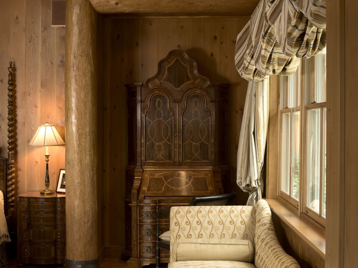 antique wardrobe against wall of log cabin next to window with billowing white curtains over setee