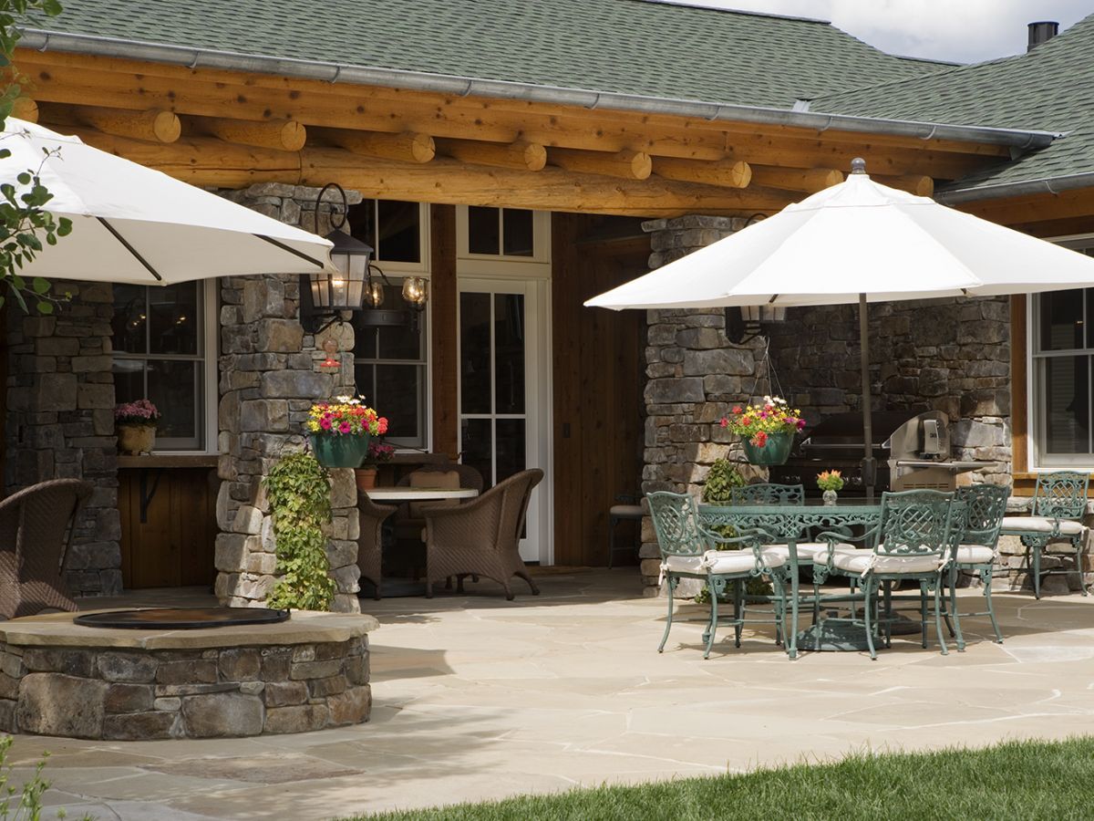 patio on back of log cabin with two tables and two white umbrellas
