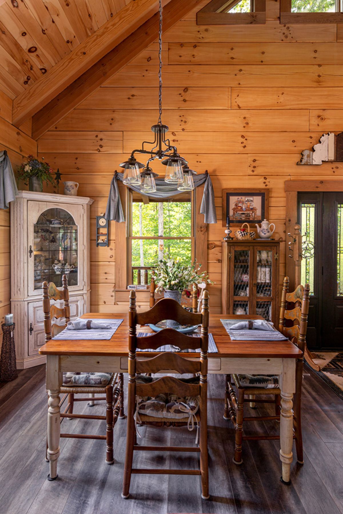 white table with butcher block top and dark wood chairs underneath chandelier light with white hutch in far left orner of room