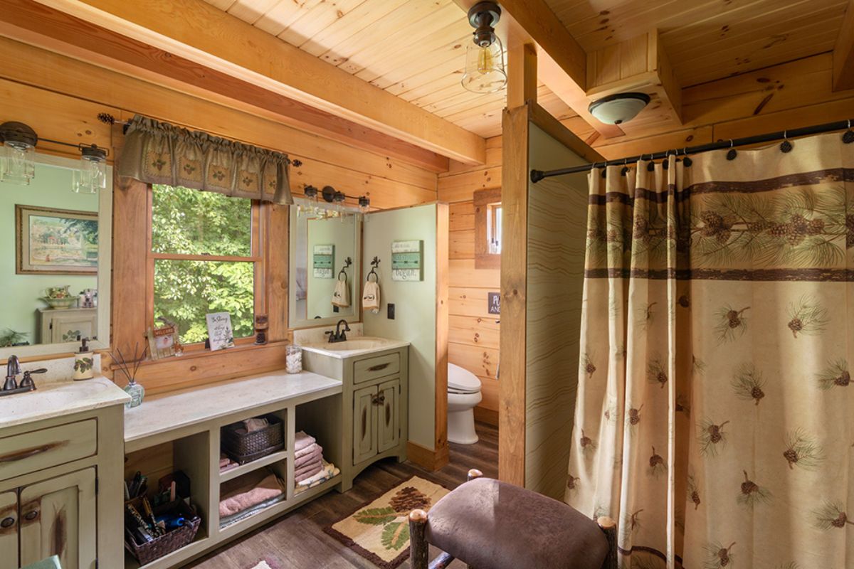 shower in right foreground with light green walls against log walls next to open shelves of vanity on left