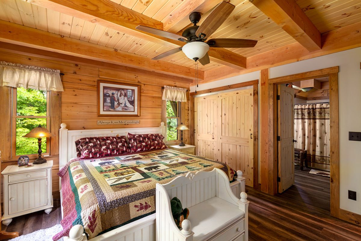 quilt on bed against log cabin wall with open door on right next to closet