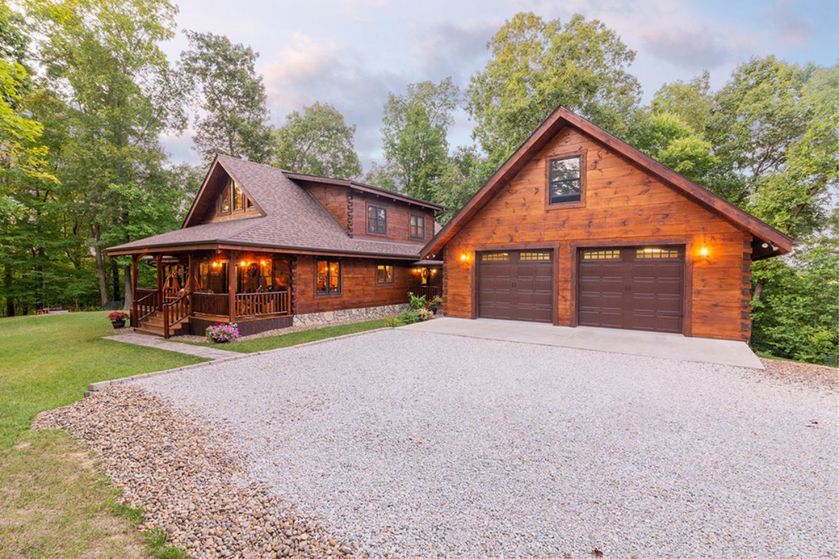 two car garage next to dark wood log cabin with covered porch