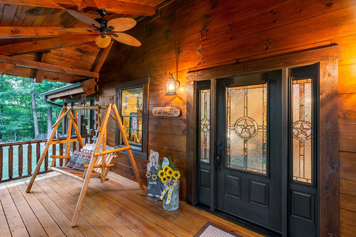 dark green door with glass panels on front of log cabin with porch swing next to door