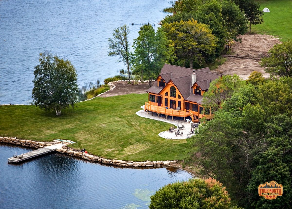 view of log cabin on edge of lake with concrete path to dock