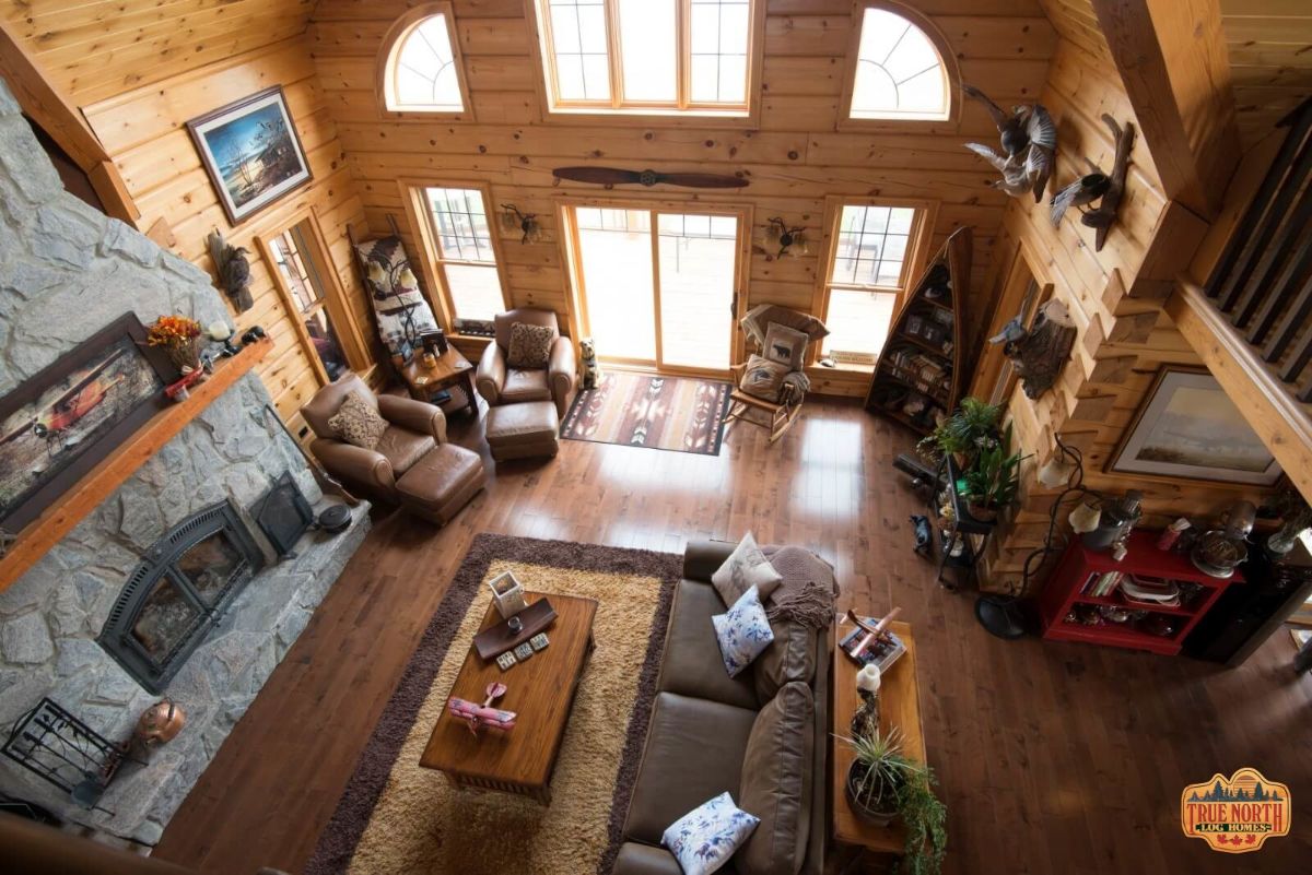 view from loft of great room with sofas on rug and chairs by wall of windows