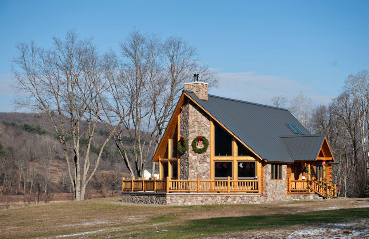 stone chimney on back side of log cabin with wall of windows on both sides