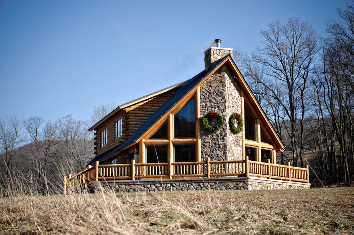 side of log cabin with stone chimney on wall with wreaths hanging on chimney