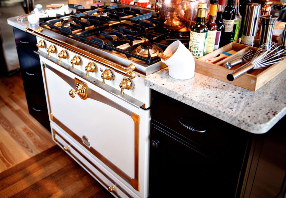 classic white stove with brass hardwarer and black gas top in dark wood cabinets with light granite countertops