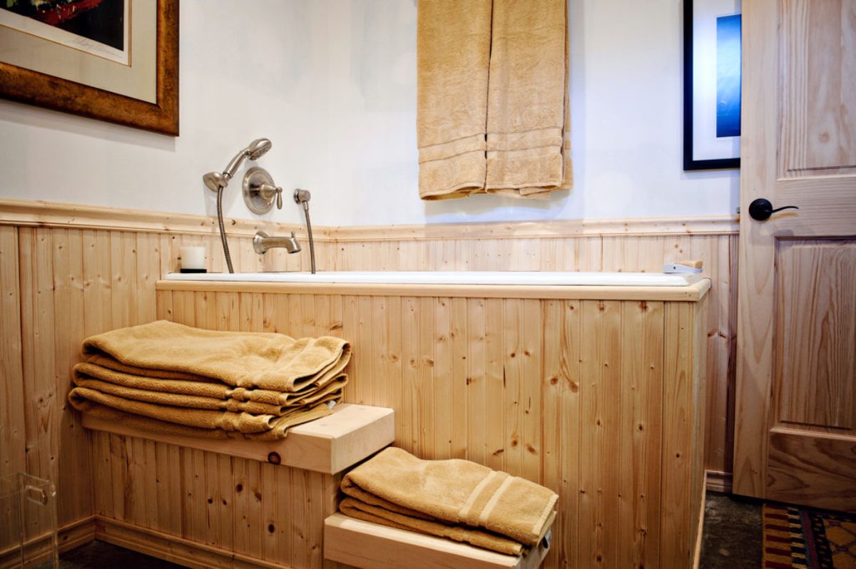 towels stacked on wooden ledge by soaking bathtub surrounded by wooden base