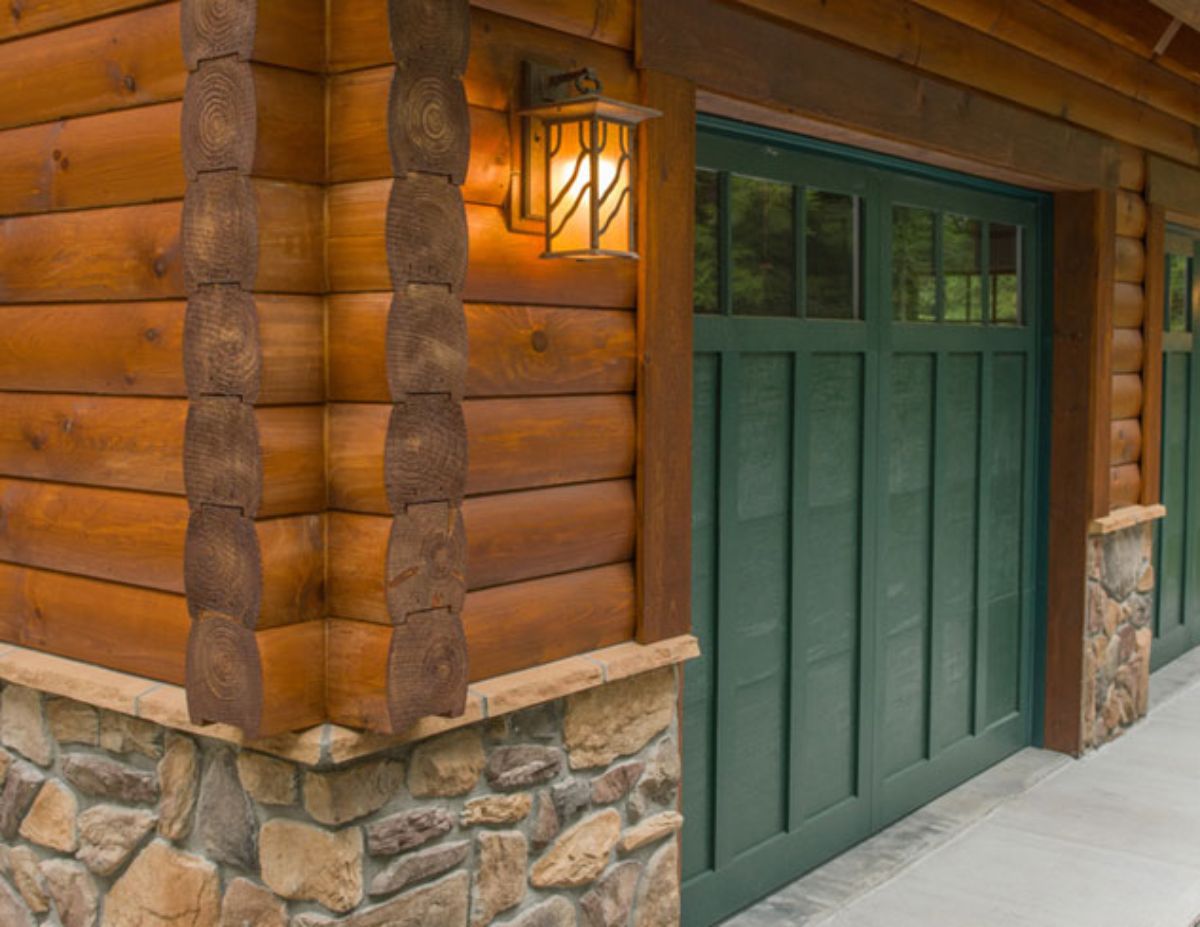 dark green garage door next to log wall with stone foundation