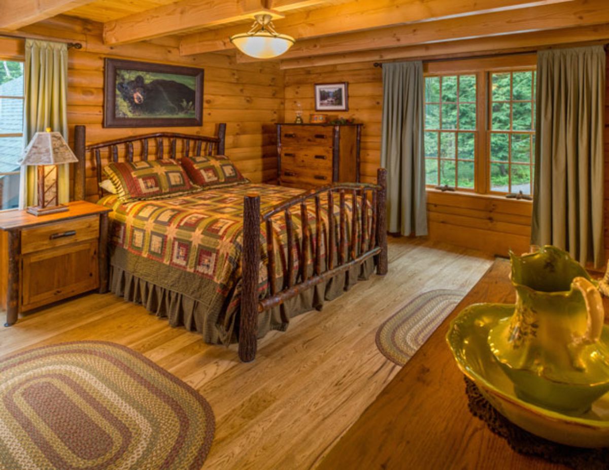 wood bedframe on bed in log cabin with wood walls and floor