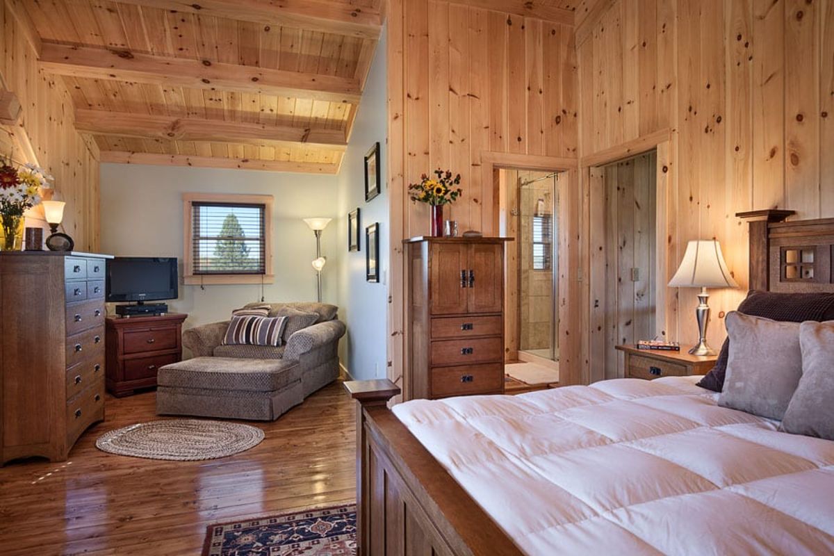 cream lounge chair in corner of log cabin bedroom with bed in foreground