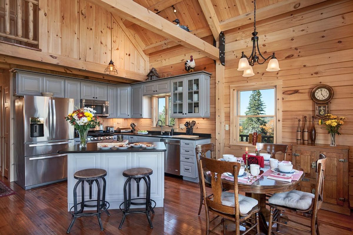 light gray cabinets on island in log cabin kitchen with brown stools next to dining table