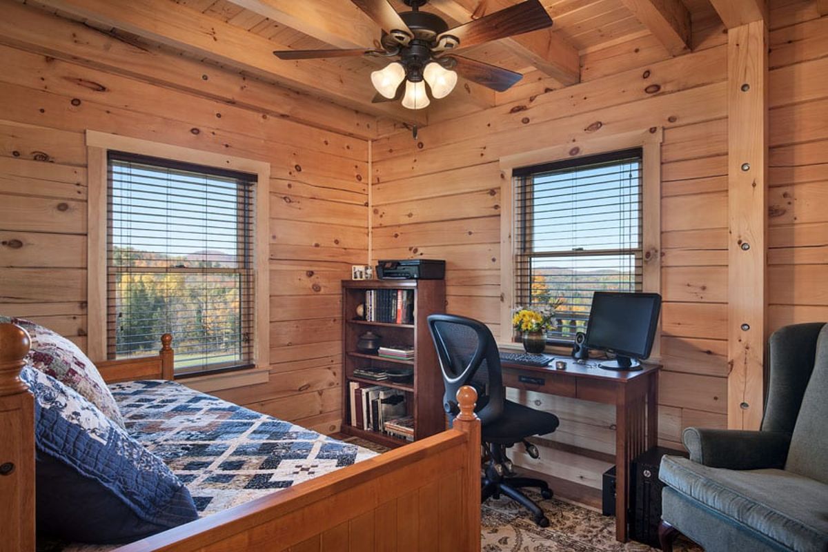 desk against wall of log cabin with bookself in far corner and bed in front corner
