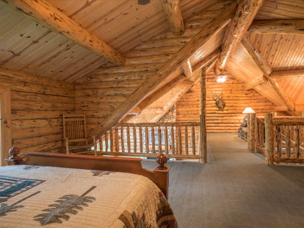 bed in corner of cabin loft with log railing on edges of space