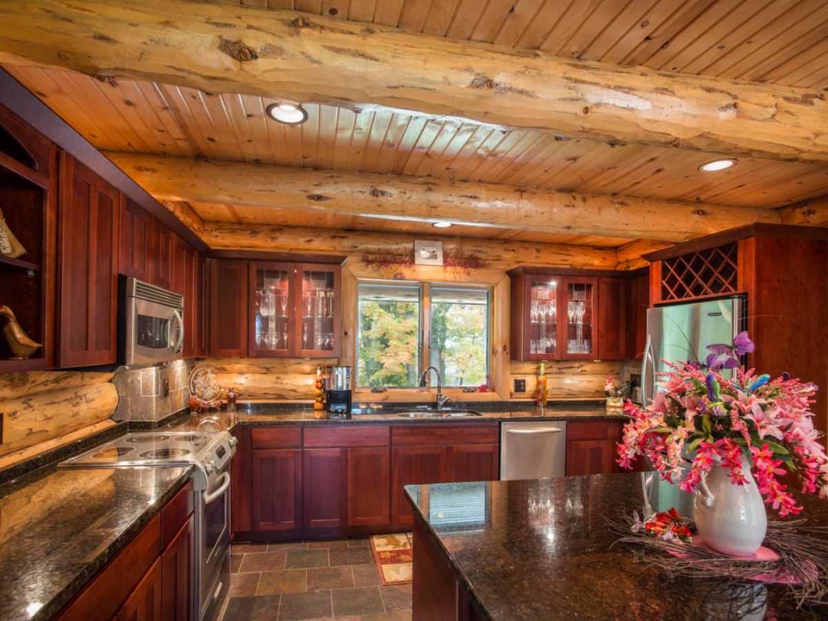 kitchen in log cabin with dark red cabinets and granite counter tops next to stainless steel appliances