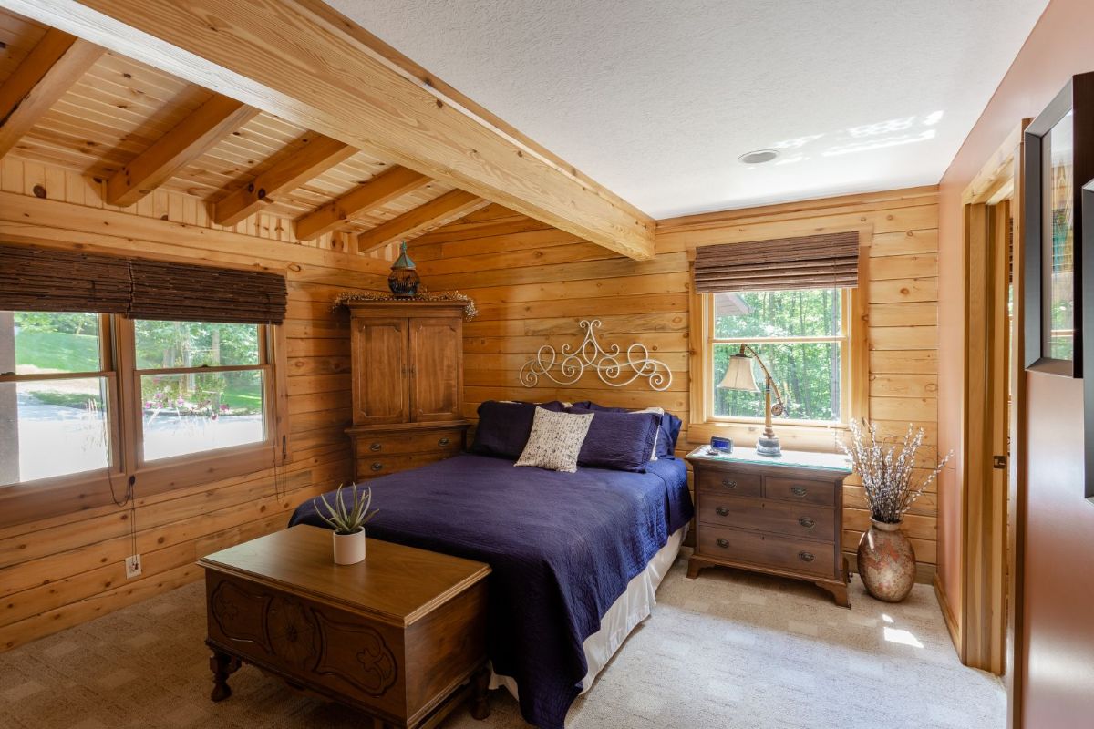 blue bedding on twin bed against wall of windows in second floor log cabin bedroom