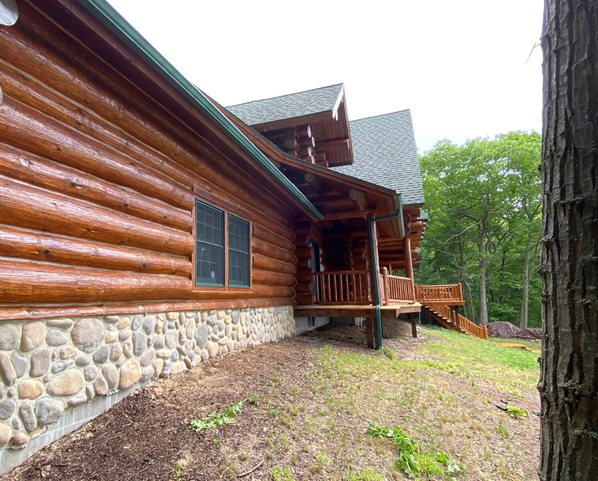 side wall of log cabin with dark stain green roof and stone foundation