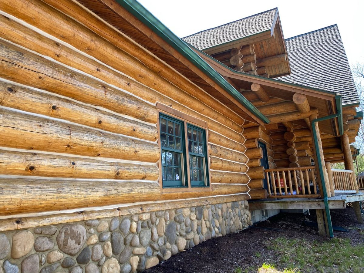 side of log cabin showing unstained log and stone foundation