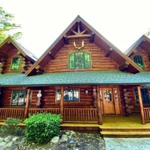 dark wood log cabin with green roof and trim front porch that is covered
