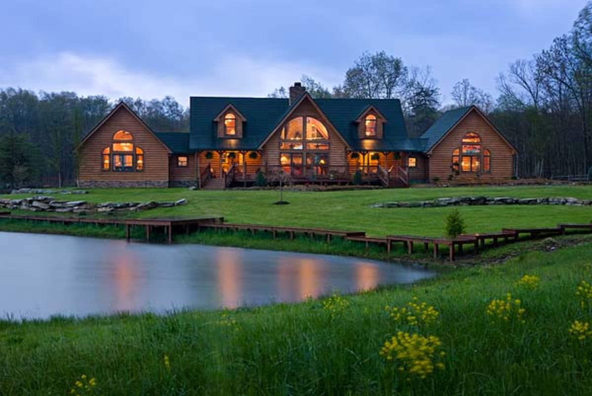 small lake by log home with sprawling ranch layout and tall green roof