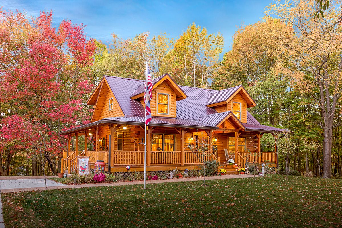 gravel driveway beside log cabin with warp around covered porch and flag pole in front yard