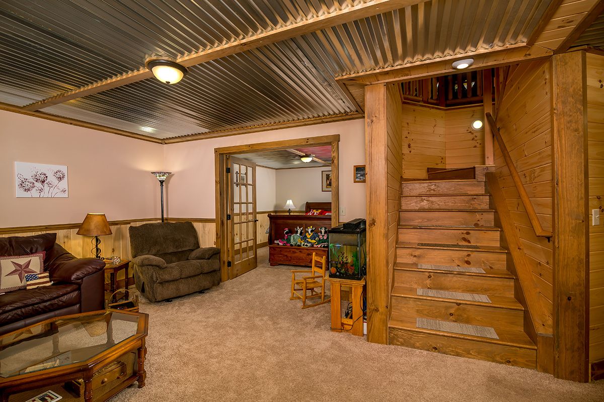 stairs leading down to basement opening into great room with sofa on left and door to bedroom on back of room