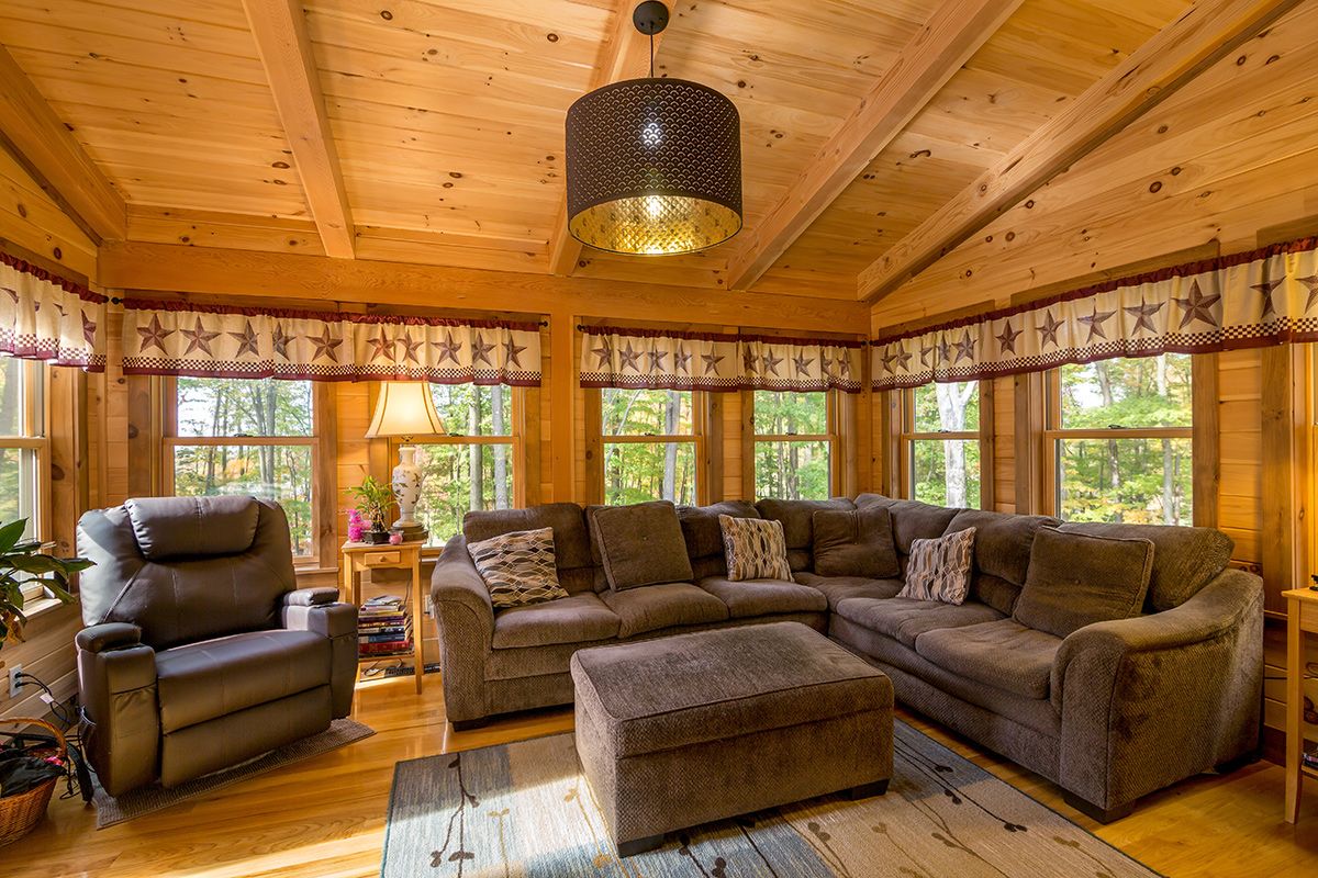 brown suede sectinal sofa against windows in log cabin with retro light fixture above