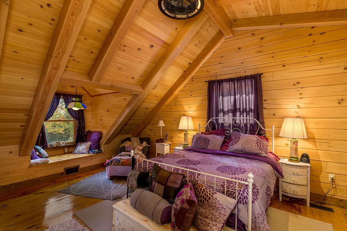 purple bedding and curtains on wrought iron bedframe in log cabin upper level bedroom