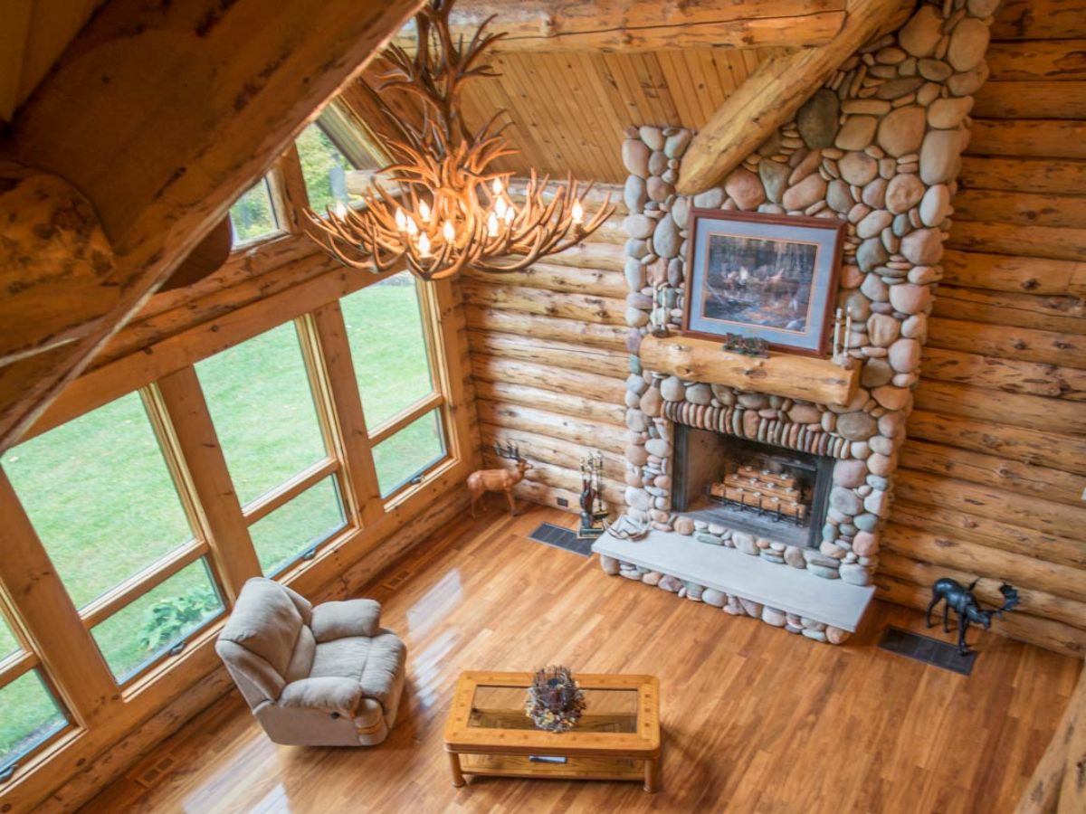 view into great room from log cabin loft showing windows on left and stone fireplace
