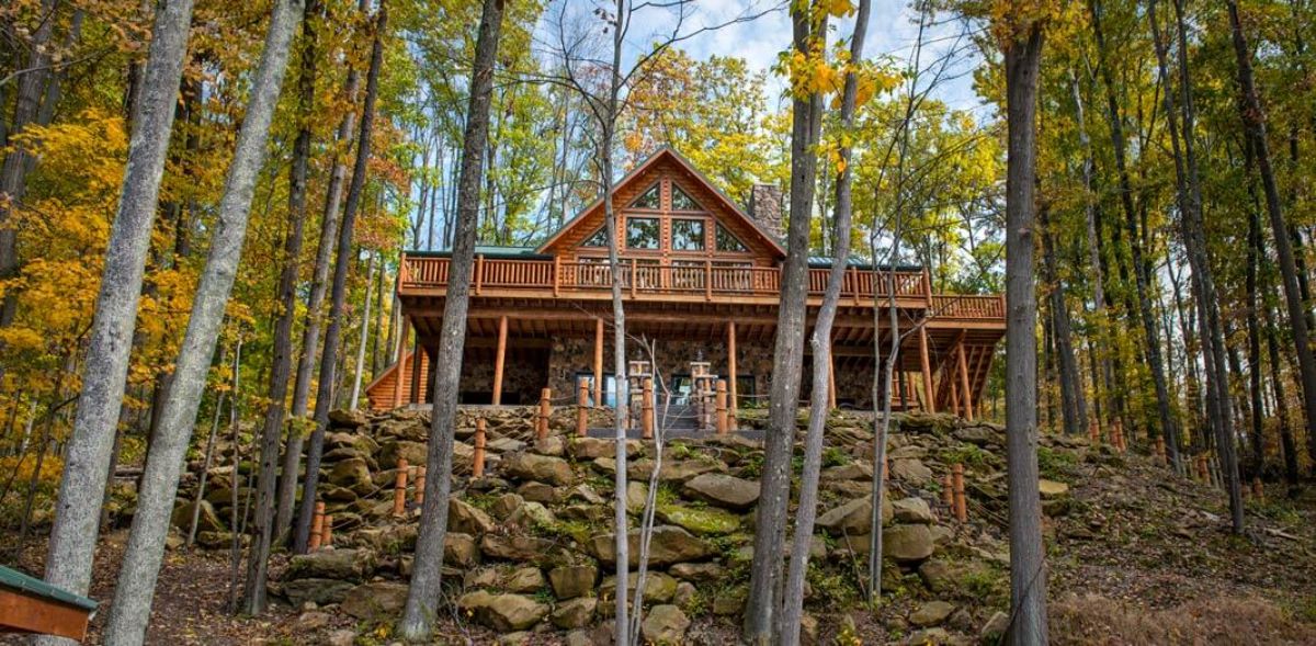 front of log cabin with two stories and rock wall in front with trees