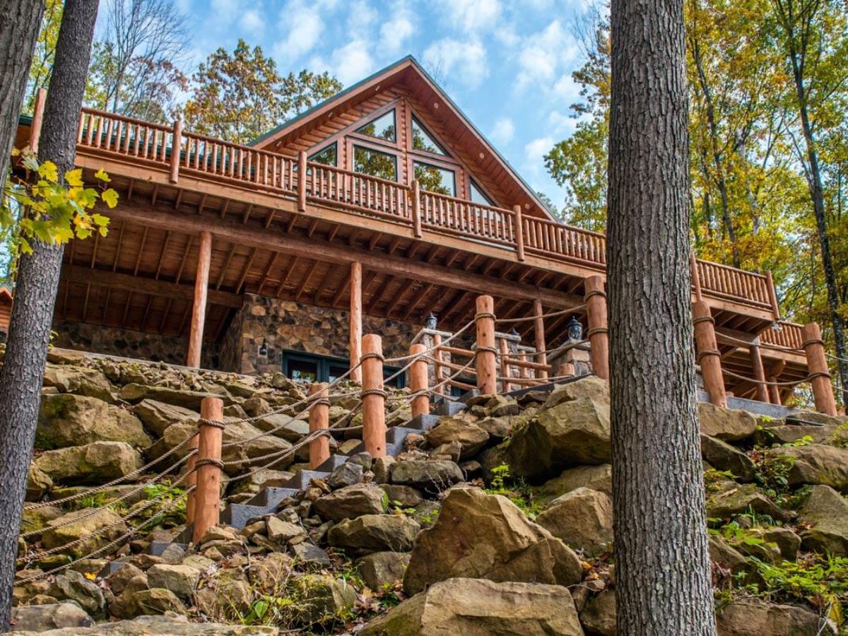 back of log cabin showing rock wall beneath deck and wood railing on walkway up path to cabin