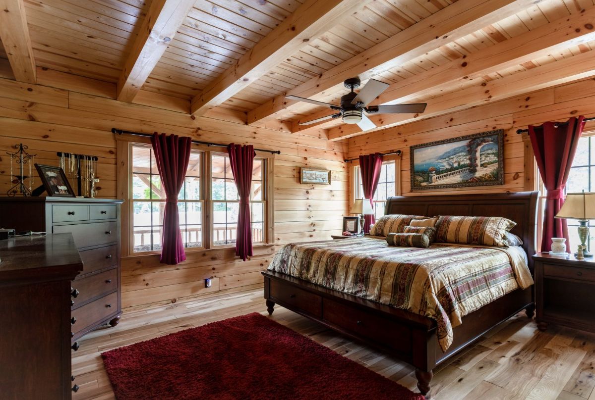 striped bedding on bed in log cabin bedroom with curtains on windows to left