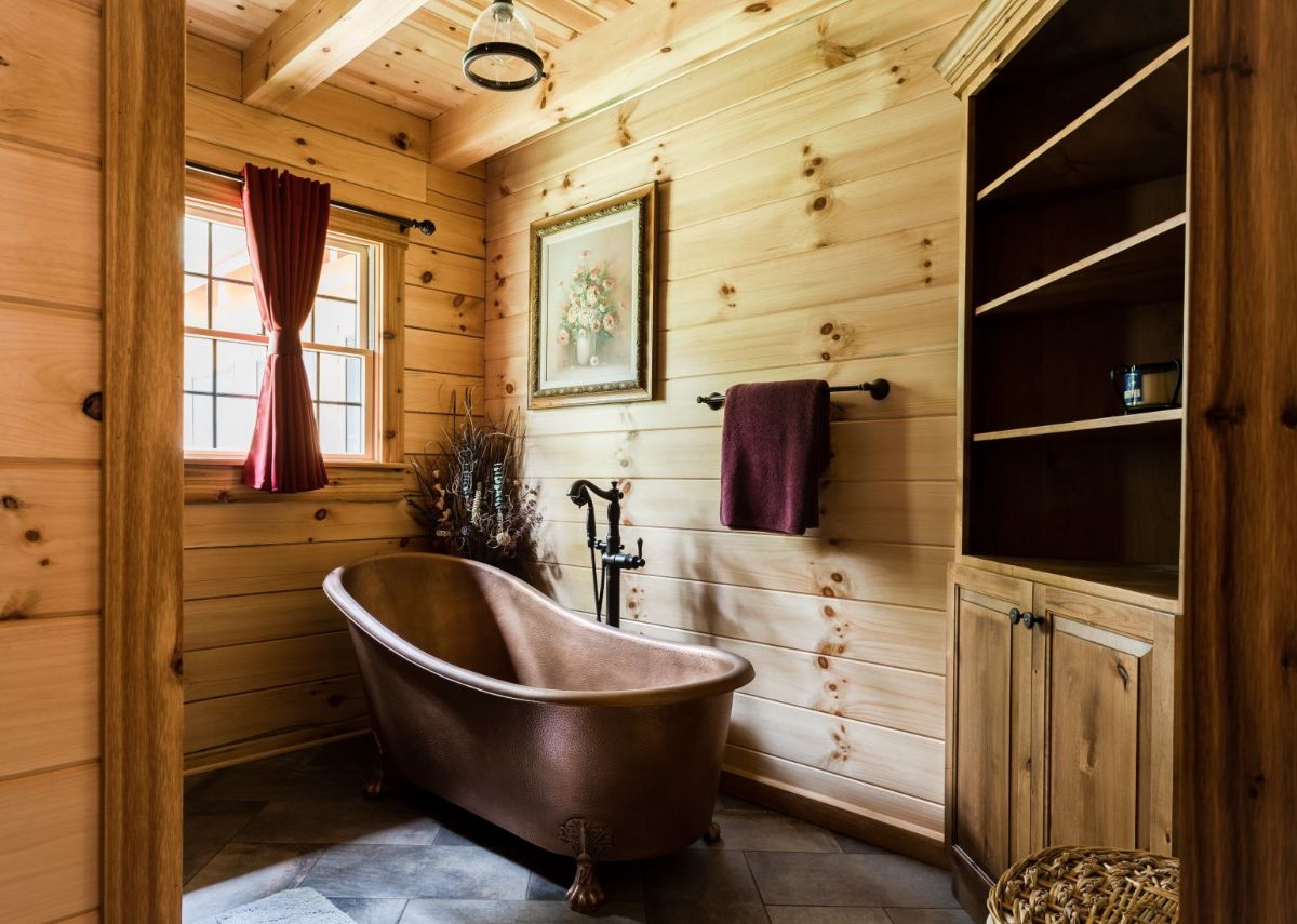 copper clawfoot bathtub against wood wall in bathroom