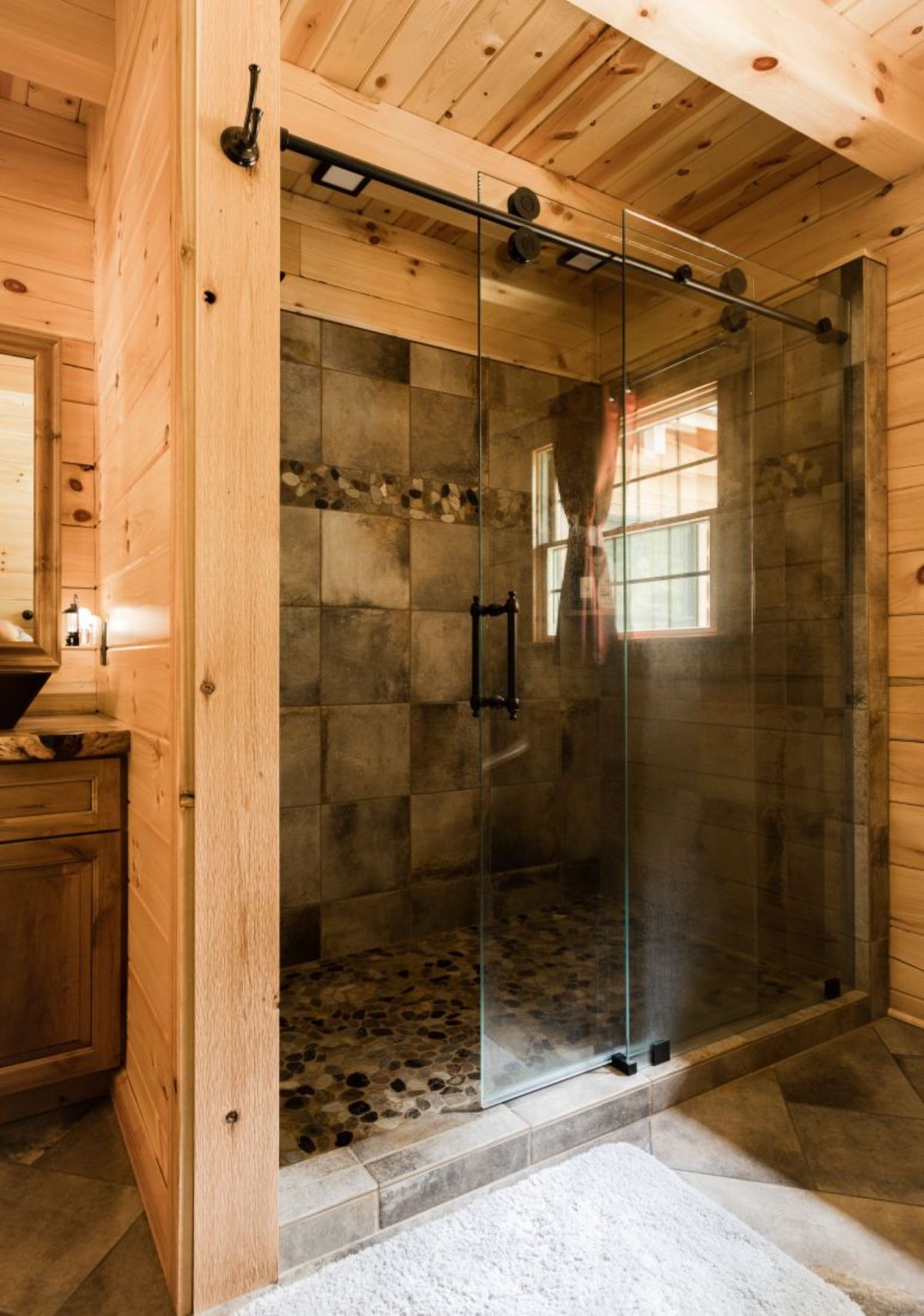 stone tiled shower with glass door in raw wood wall