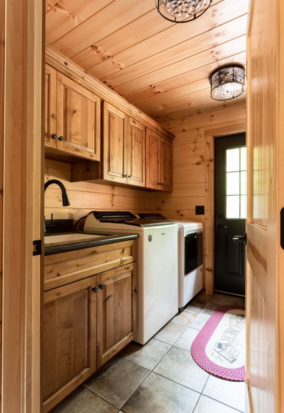 white washer and dryer against wall by dark door with light wood cabinets all around in cabin