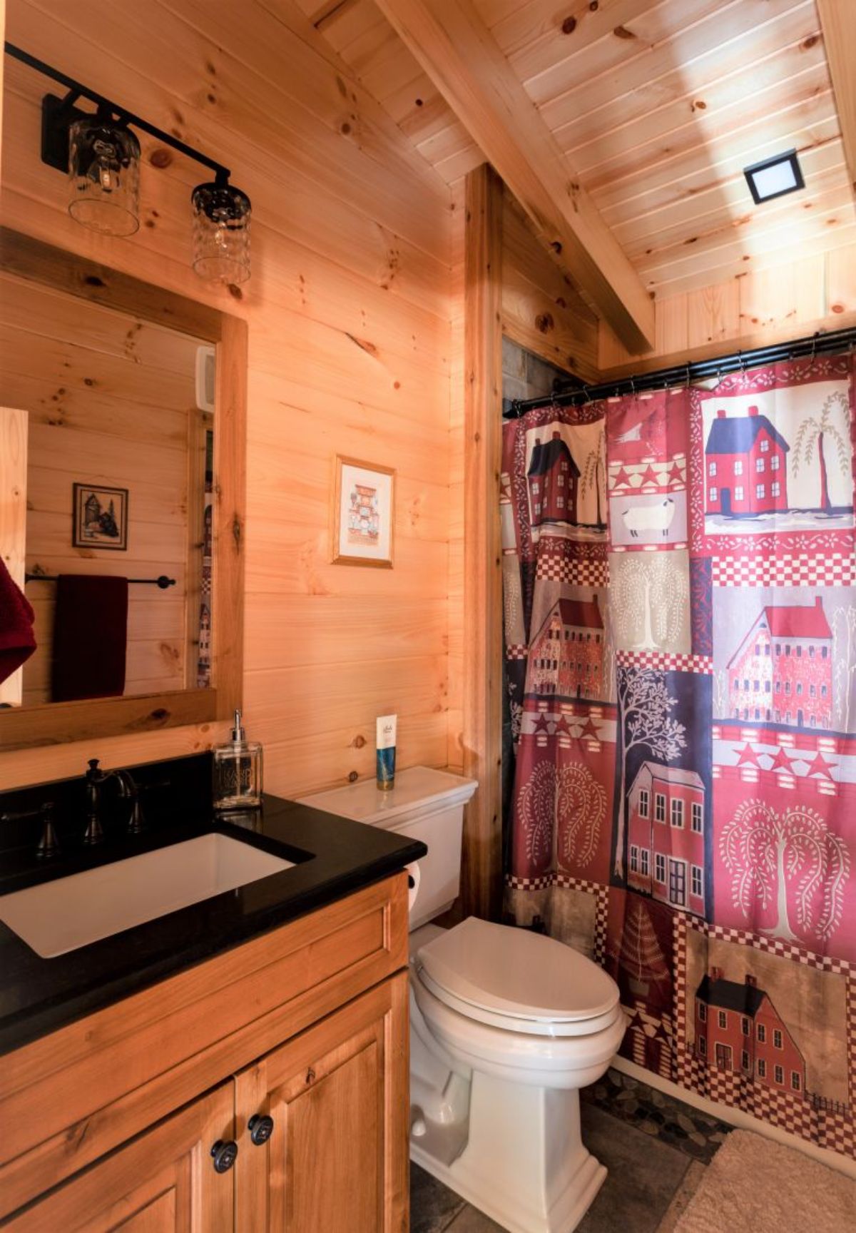 rustic blue and red shower curtain beside white toilet in bathroom with black countertop and white sink