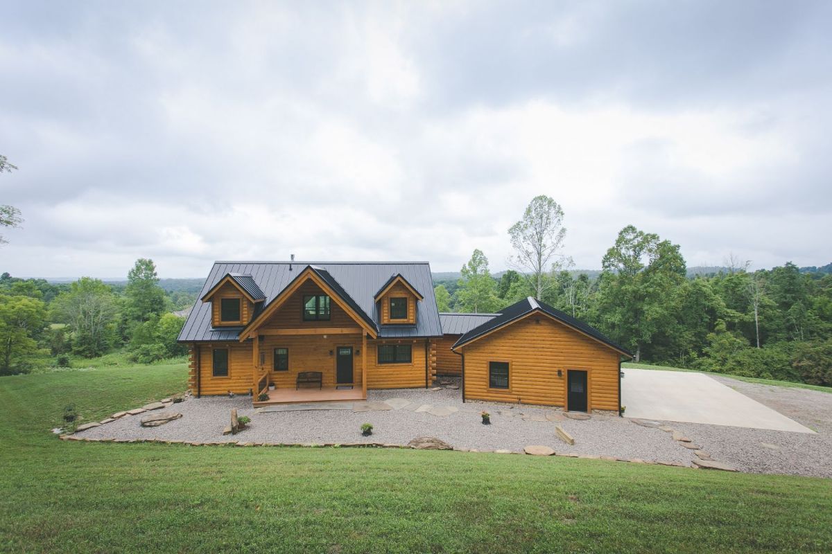 log cabin ith attached garage and three dormer windows on gravel lot