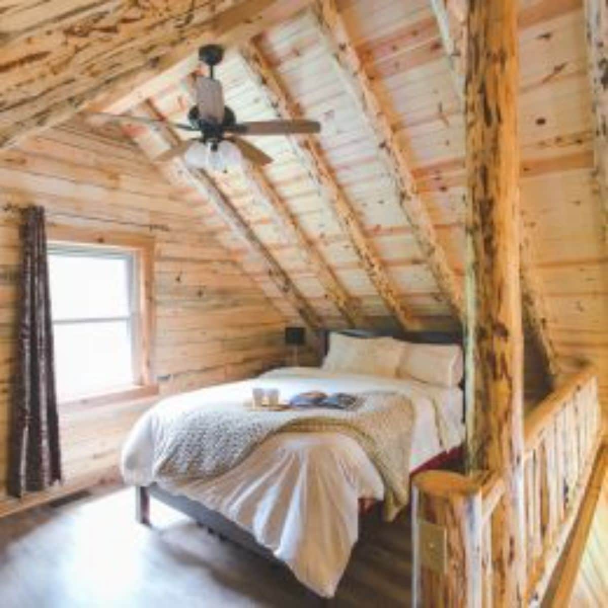 bed next to railing of loft with ceiling fan above